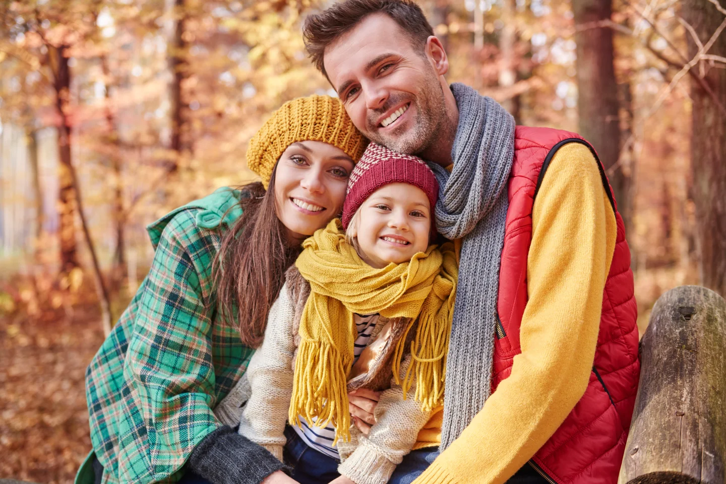 Eltern und Kind sitzen eng beieinander zwischen bunten Herbstbäumen