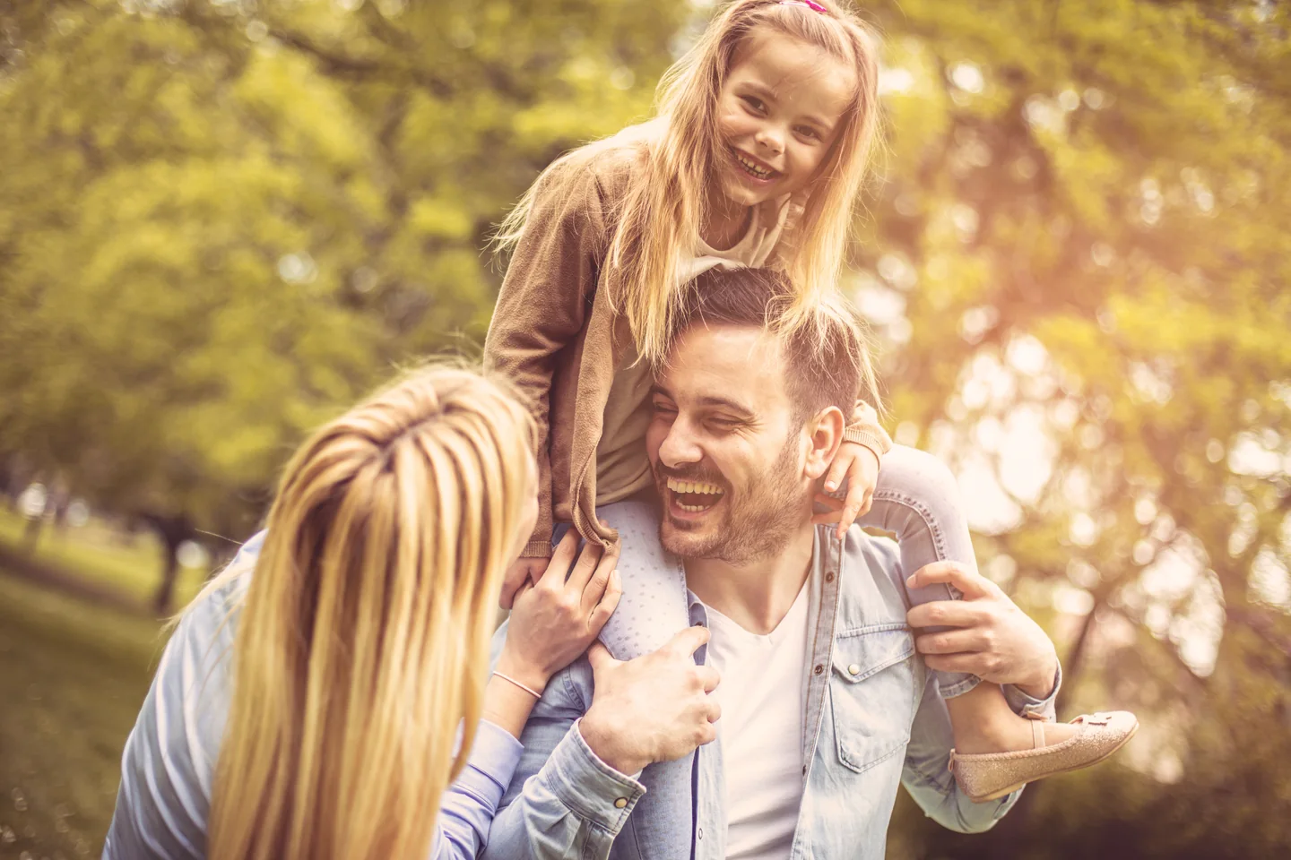 Eine Familie lacht gemeinsam im warmen Licht zwischen Bäumen